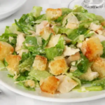 Caesar salad served on white plate with silverware