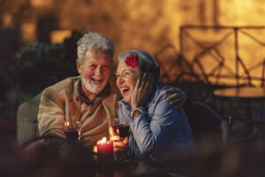 Beautiful senior couple sitting outdoors in a romantic roof restaurant. Two glasses of red wine to celebrate a positive moment.
