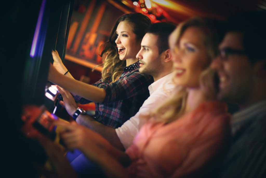 Group of young adults in mid 20's playing slots in a casino, winning and having fun. Two couple on double date enjoying weekend night. Cheering, laughing..