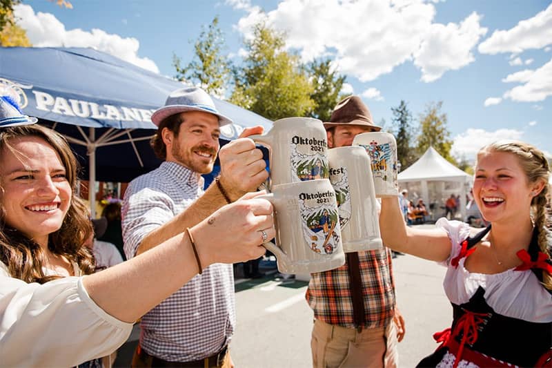 Four friends standing outside toasting steins in Colorado Springs Oktoberfest