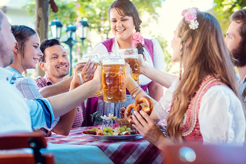 Group of friends celebrating Oktoberfest at a table with a waitress pouring beer.