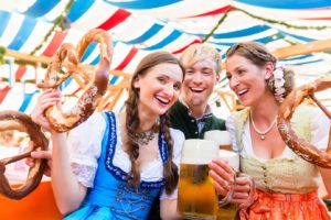 Two women and a man holding pretzels and beer celebrating Oktoberfest