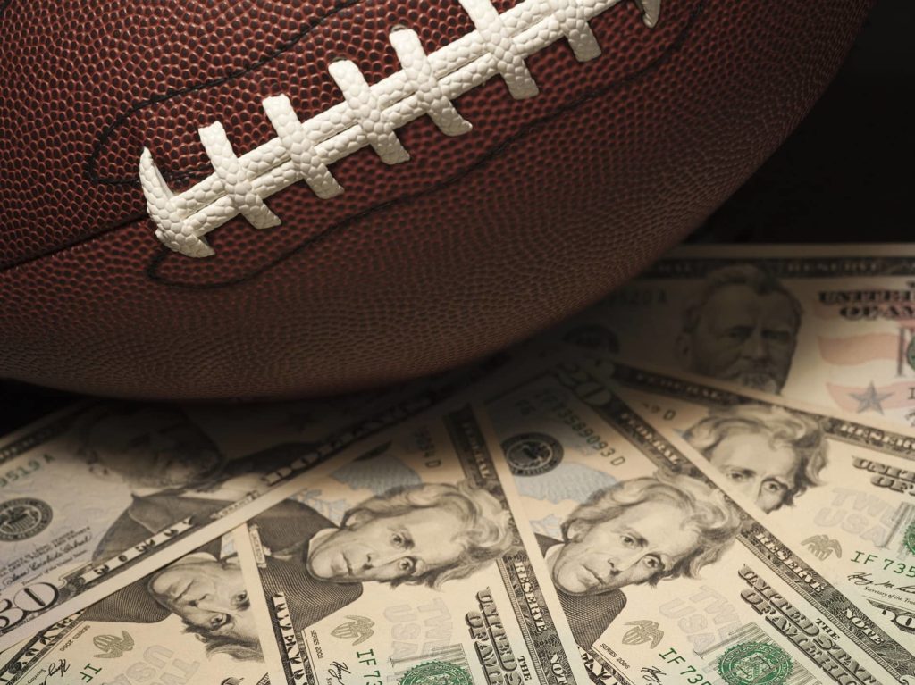 Image of an American Football laying across piles of cash representing NFL Betting