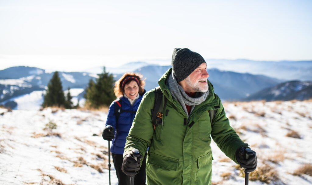 Senior couple with nordic walking poles hiking in snow-covered winter nature, healthy lifestyle concept.