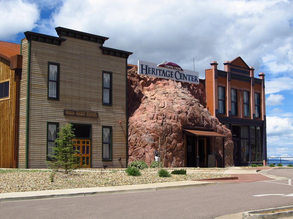 A view of the Heritage Center in Cripple Creek from across the street - a red brick building with black trim flanks a natural stone organic shaped building, and a flat front early 20th century wood building flanks the left. 