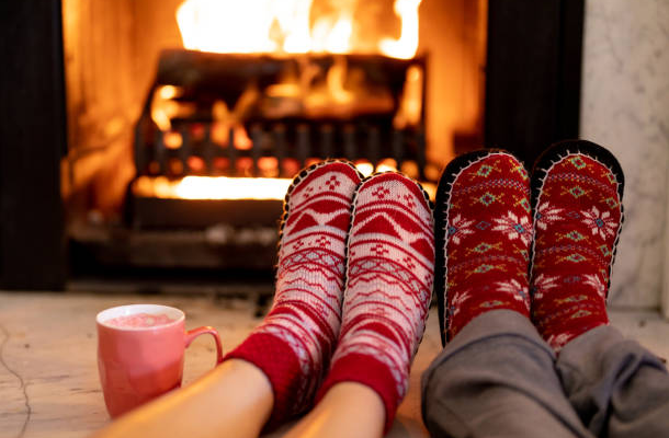 A view of two sets of knit-sock clad feet stretched out in front of a lit fireplace
