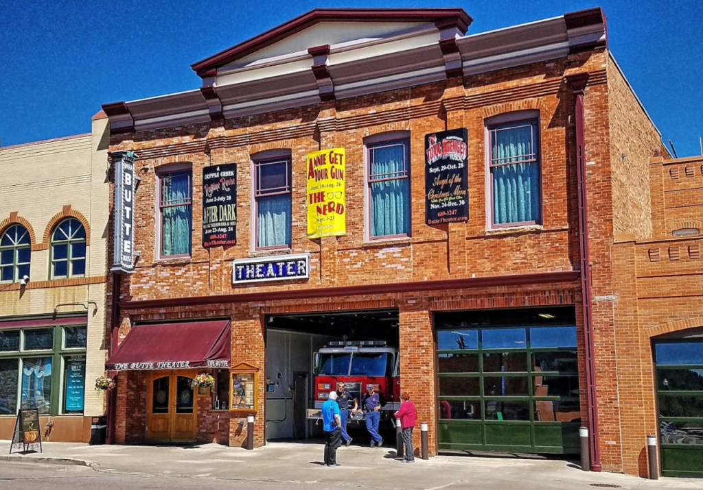 The Butte Theater is shown - a brick historical building that used to serve as a fire station with garages on the bottom floor and one open garage revealing a red fire engine