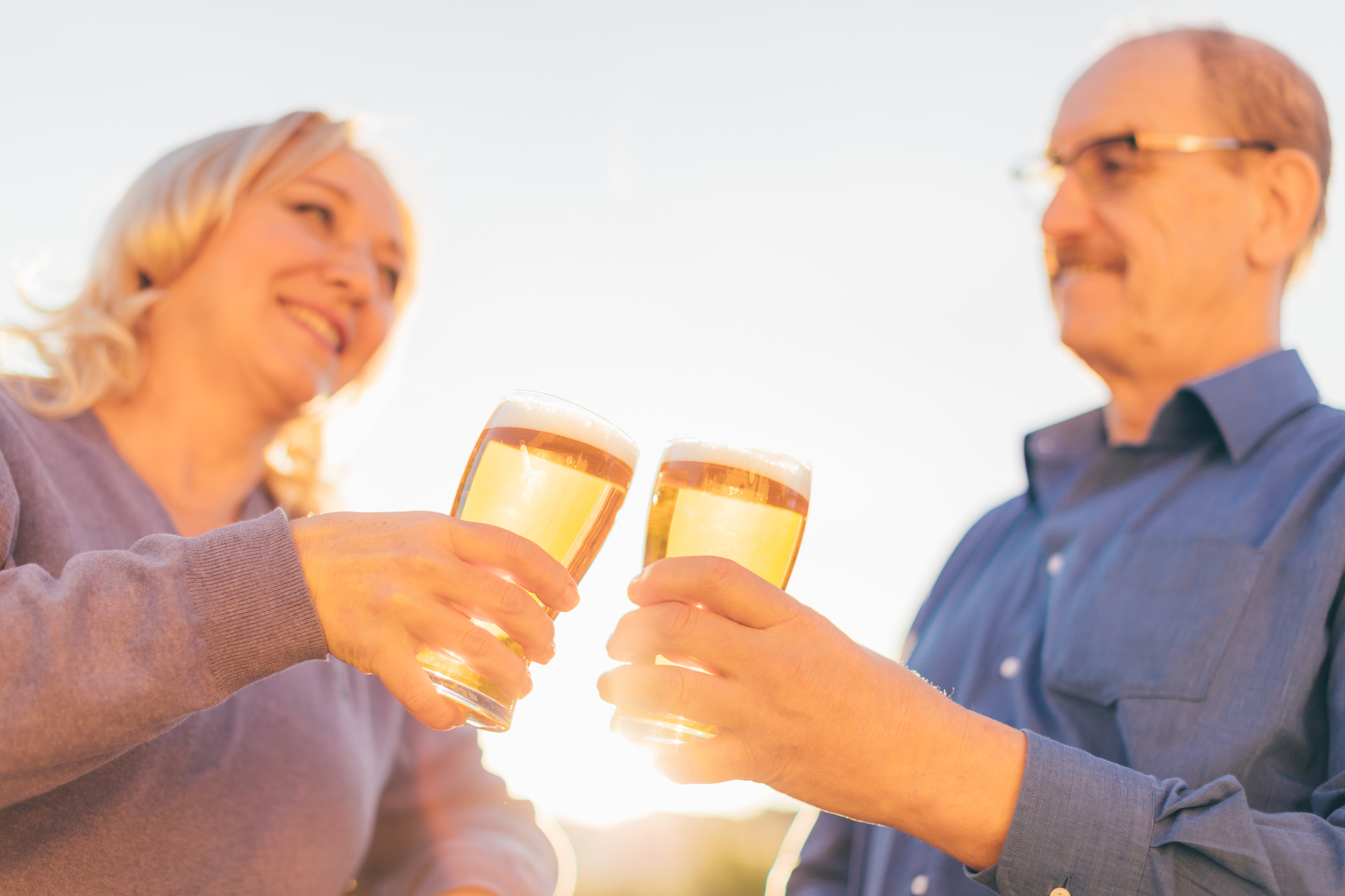 Senior couple drinking beer together, focus on hands with glasses.