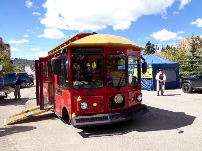 A red trolley sits parked with its nose facing the viewer on a beautiful sunny day.