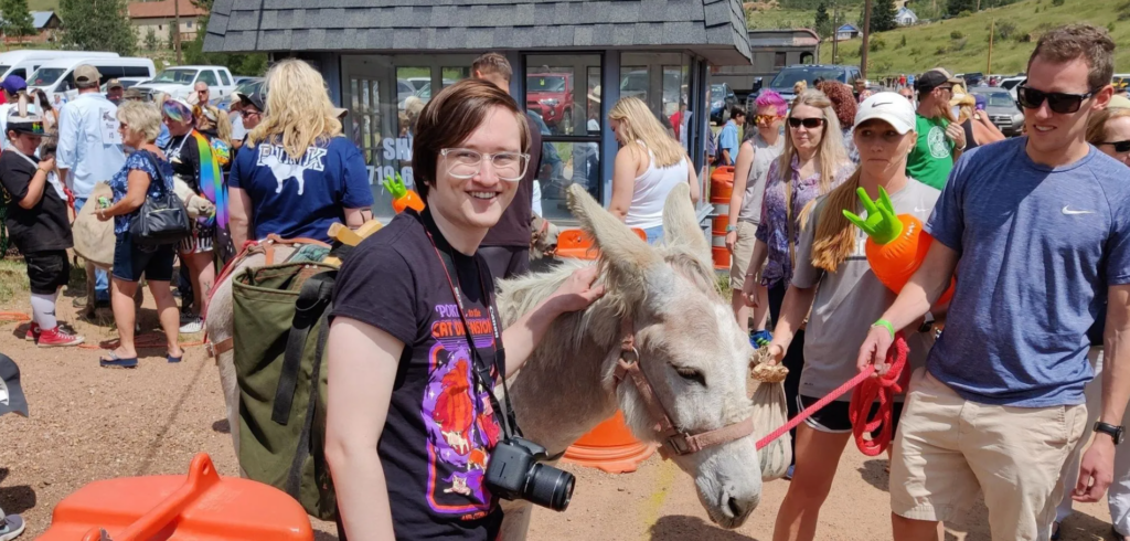 Teen standing with a camera in front of crowd petting a donkey