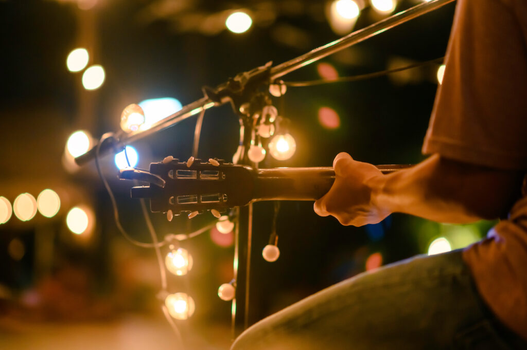 Rear view of the man sitting play acoustic guitar on the outdoor concert with a microphone stand in the front, musical concept.