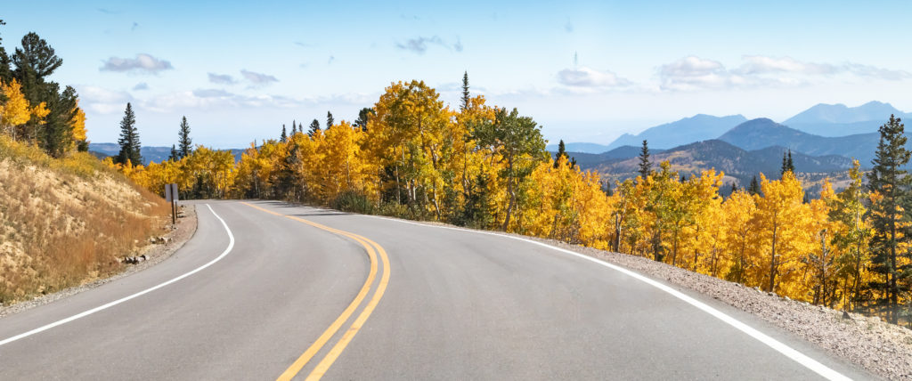 Empty road winds through a panoramic mountain landscape scene with golden fall aspen trees in the Colorado Rocky Mountains