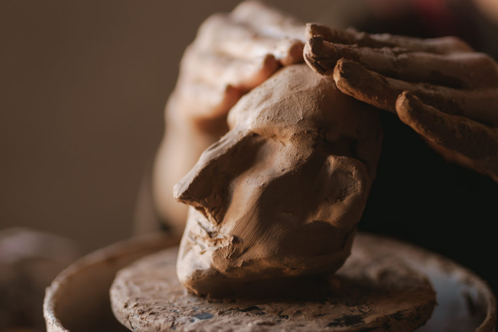 Woman sculptor artist creating a bust sculpture with clay in an art studio close up