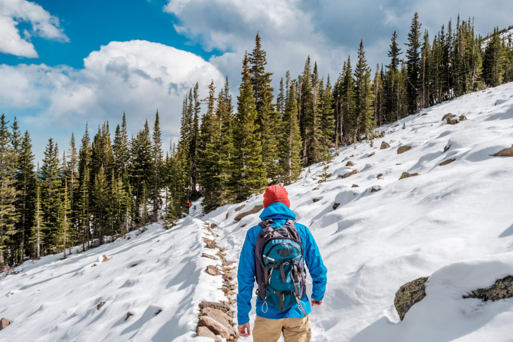 Tourist with backpack hiking on snowy trail in Rocky Mountain National Park, Colorado, USA.