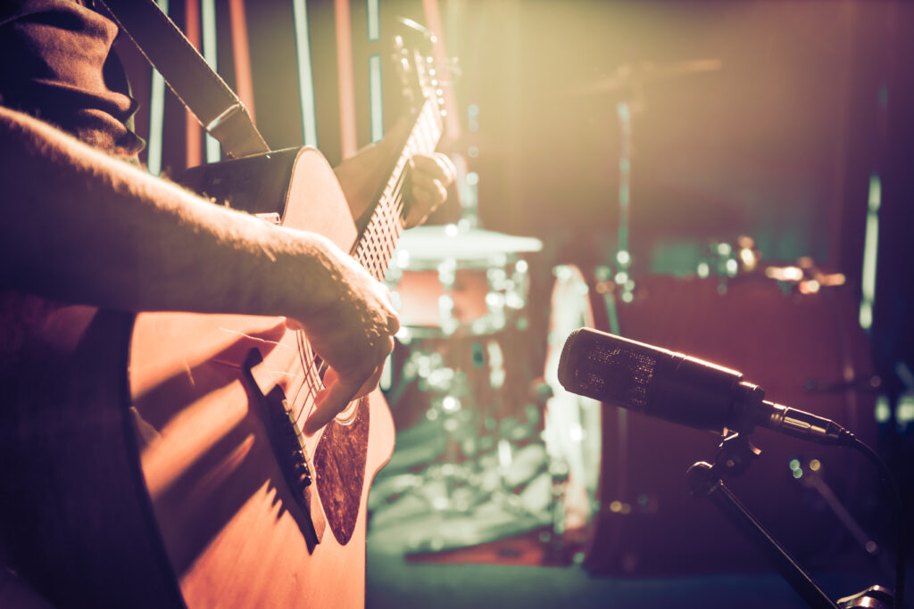 The Studio microphone records an acoustic guitar close-up, in a recording Studio or concert hall, with a drum set on a background in out-of-focus mode. Beautiful blurred background of colored lanterns