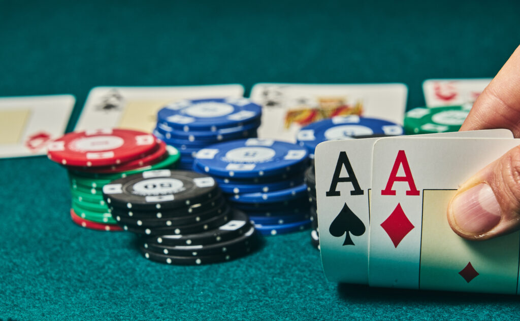 close-up of two aces held in one hand on the green game mat on the right side of the image to leave room for editing, other cards and poker chips are on the mat